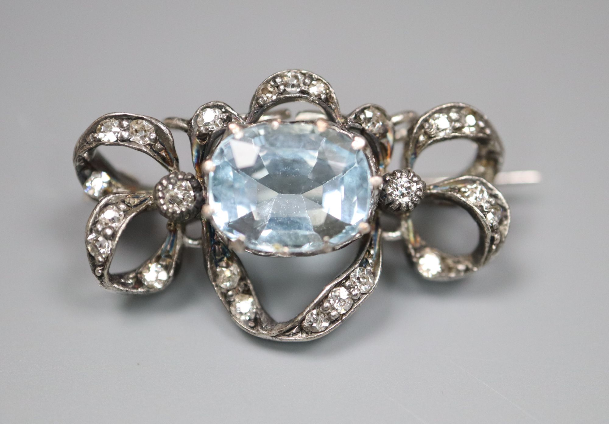 An Edwardian white metal, aquamarine and diamond set scroll brooch, 25mm, gross 3.8 grams.